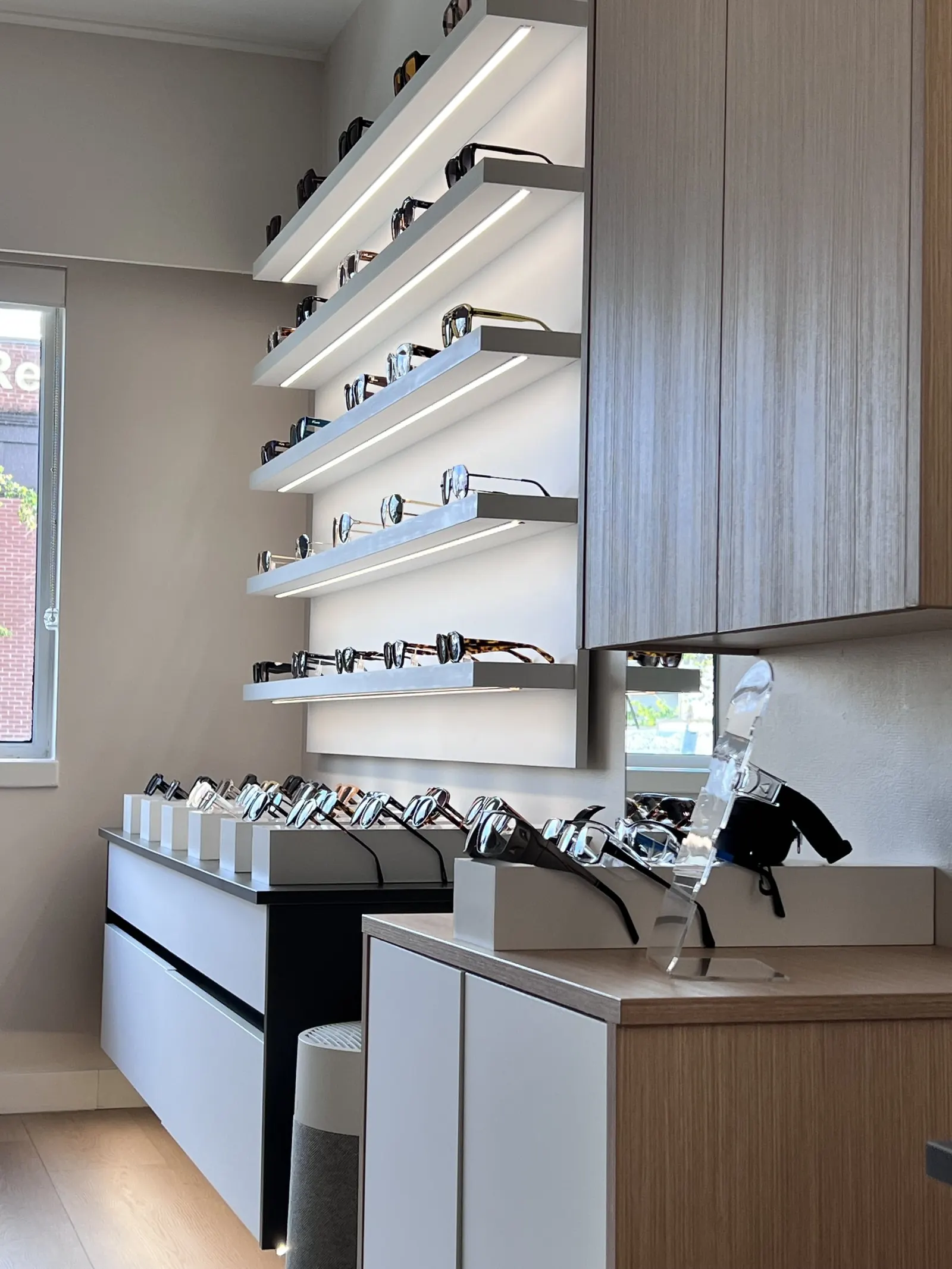 A backlit wall of sunglasses above a row of frames on white display blocks